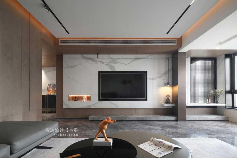 設計師巧妙地運用色彩和燈光，把看似獨立的空間完全打開并融于整體。木色的護墻、簡潔的裝飾、大理石電視背景以及擺放家具中夾雜的跳色的點綴，將原本素雅大氣的空間變得有了些許生活氣息。